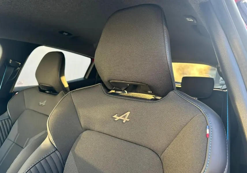 Gros plan sur les sièges avant noirs avec logo Alpine et surpiqûres bleues dans une Renault Clio V rouge flamme.