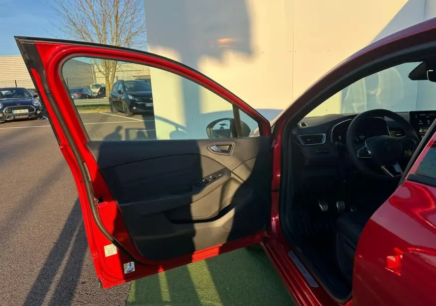 Vue côté gauche avant de la Renault Clio V rouge flamme avec porte ouverte et intérieur noir visible au soleil.