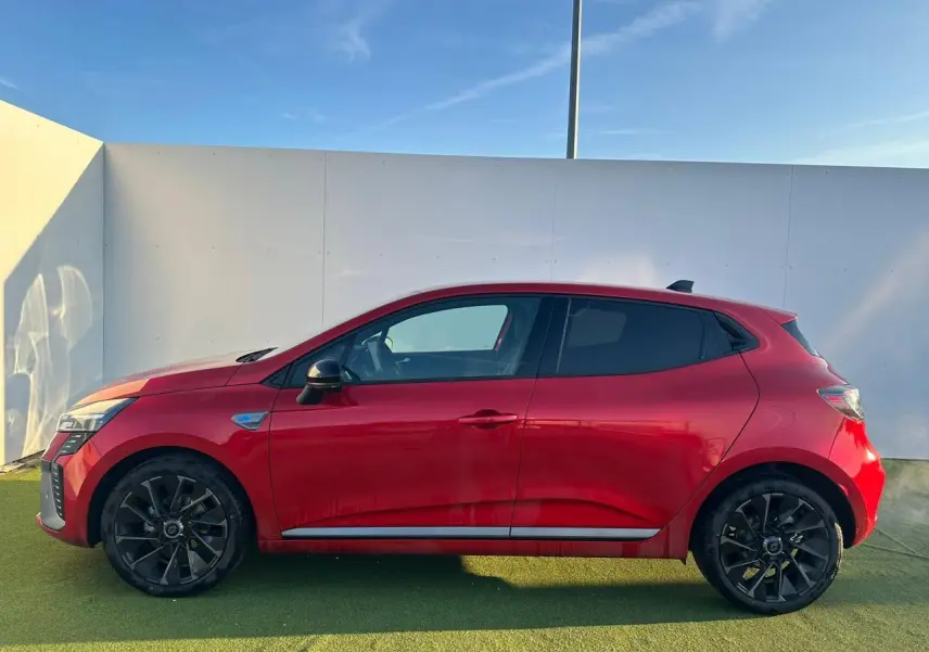 Profil côté gauche d'une Renault Clio V rouge flamme métal avec jantes alliage noires et antenne requin noire.