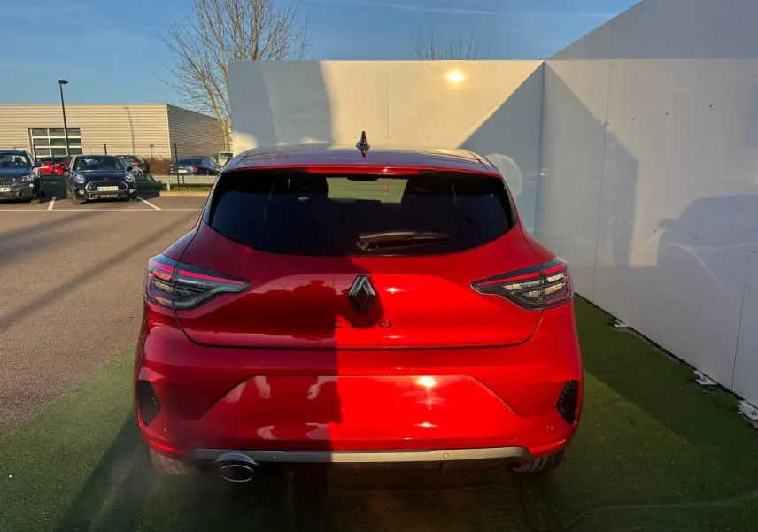 Vue arrière d'une Renault Clio rouge flamme métal avec feux LED en forme de C et antenne requin noire.