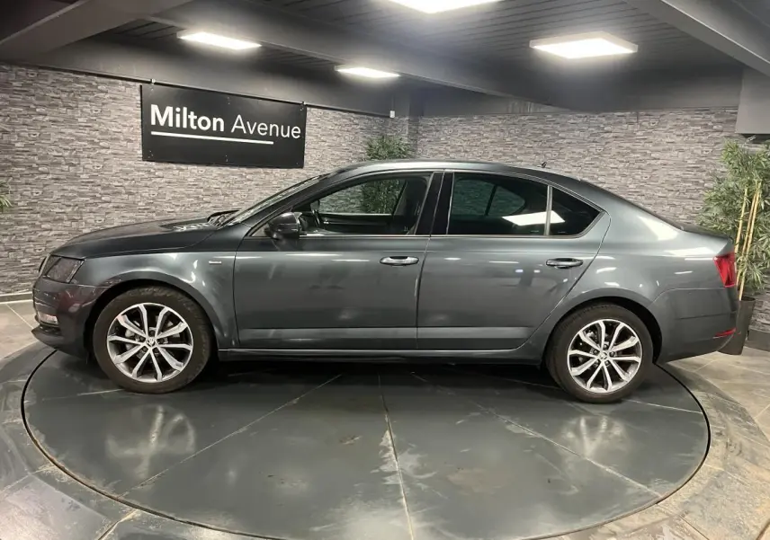 Profil côté gauche d'une Skoda Octavia gris métallisé 2020 en berline, avec jantes alliage 17 pouces, en intérieur showroom.