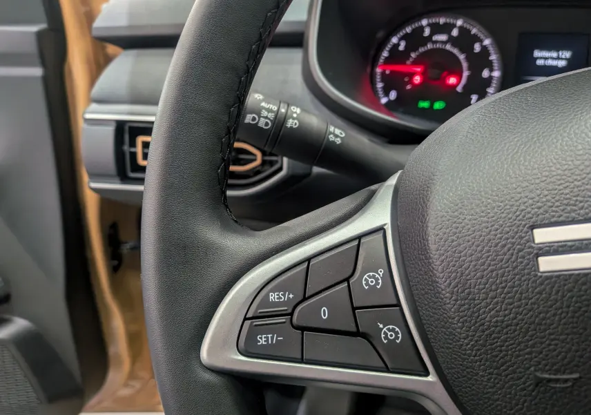 Gros plan sur le volant noir et tableau de bord du Dacia Sandero Stepway beige Safari, avec commandes de régulateur de vitesse.