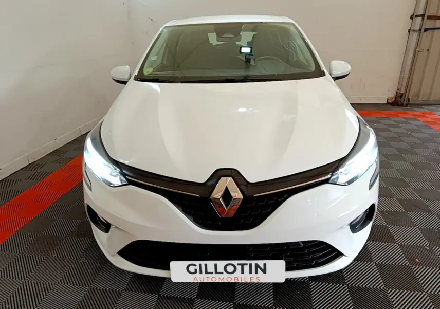 Vue frontale d'une Renault Clio blanche 2020 avec phares LED allumés dans un garage au sol carrelé noir et rouge.
