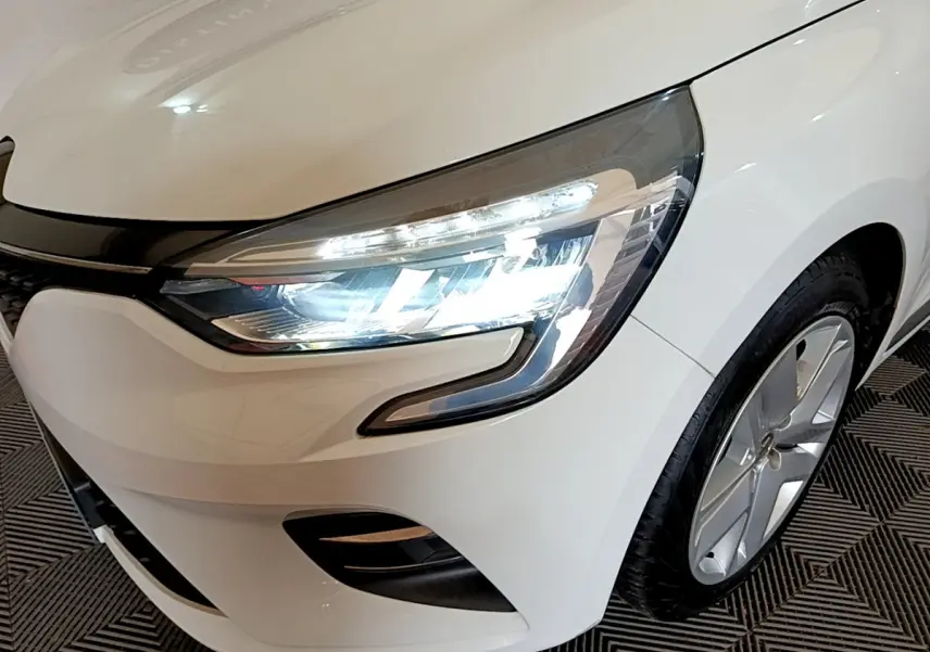 Gros plan sur l'avant droit blanc d'une Renault Clio 2020, mettant en valeur le phare LED allumé et la jante alu.