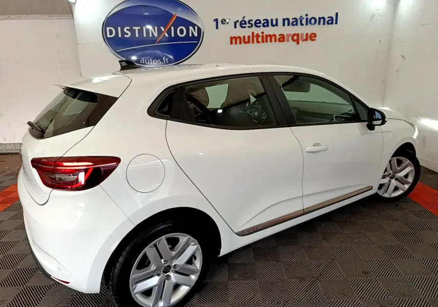 Vue de profil côté droit d'une Renault Clio Business Blue dCi 85 blanche en intérieur avec feux arrière allumés.