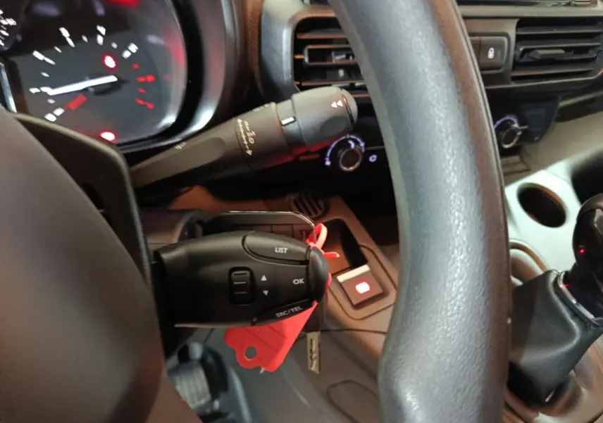 Gros plan sur le volant et commandes au volant du Citroën Berlingo blanc, avec tableau de bord et levier de vitesses visibles.