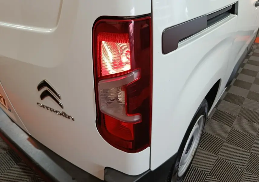 Feu arrière droit allumé d'un Citroën Berlingo blanc, vue rapprochée du côté arrière droit avec logo visible.
