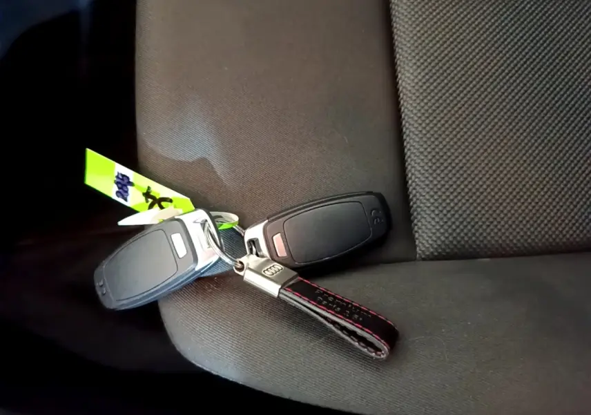 Clé Audi avec porte-clés cuir noir et surpiqûres rouges posée sur un siège tissu gris foncé.