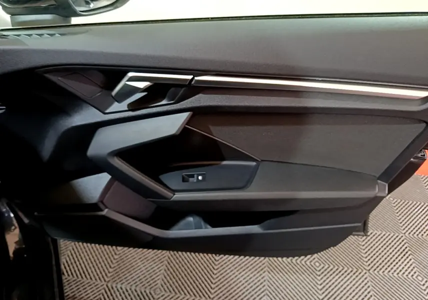 Vue rapprochée de la porte intérieure côté gauche d'une Audi A3 gris foncé, avec poignée et commande de vitre.