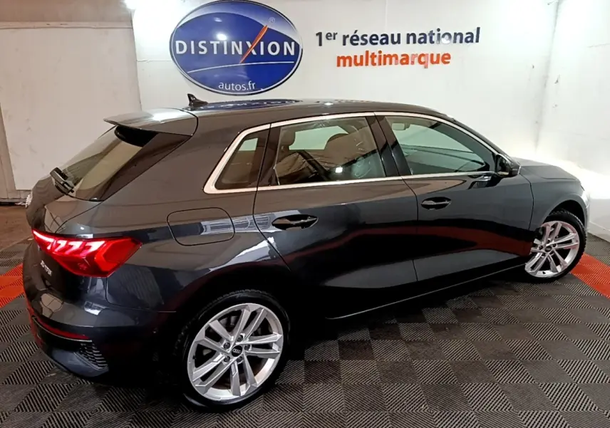 Audi A3 35 TFSI gris foncé vue 3/4 arrière droit en intérieur avec jantes alliage et feux LED allumés.