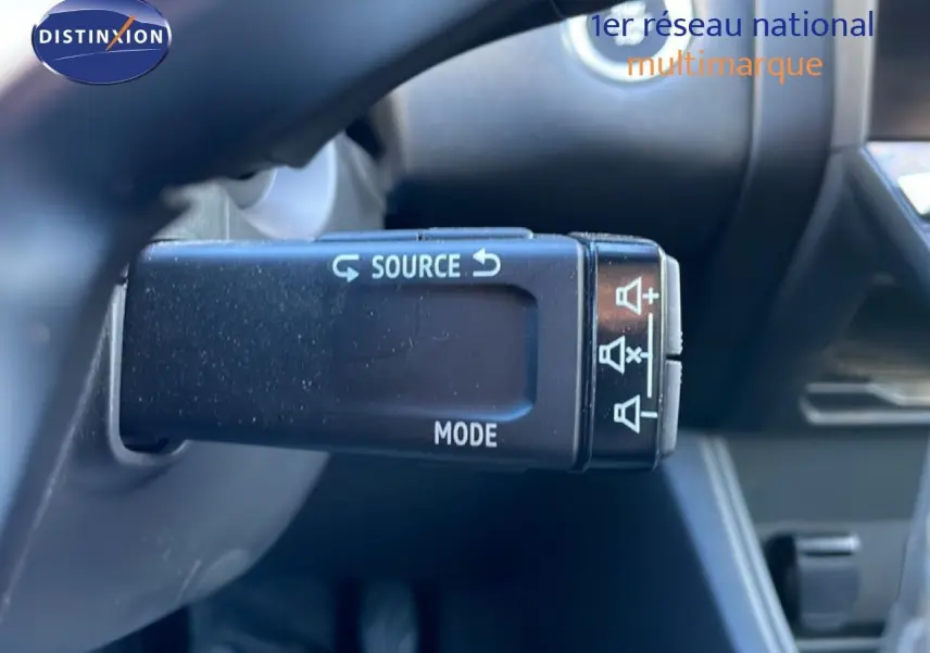 Gros plan sur la commande au volant du Renault Captur rouge désir métal avec toit noir, montrant les boutons source et mode.