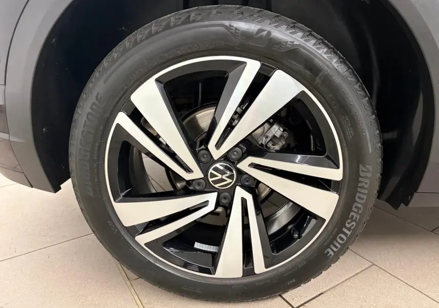 Gros plan sur la roue avant droite du Volkswagen T-Roc noir intense, mettant en valeur la jante alliage bicolore et le pneu Bridgestone.