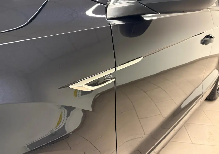 Vue latérale côté gauche du Volkswagen T-Roc noir intense, mettant en valeur l'emblème R-Line sur l'aile avant.