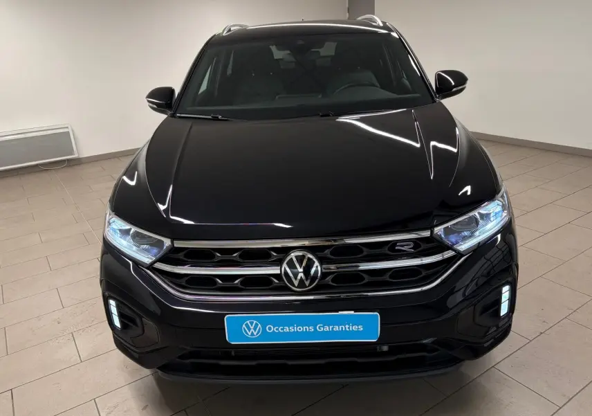 Volkswagen T-Roc noir intense vue de face, avec calandre chromée et phares LED allumés dans un intérieur neutre.