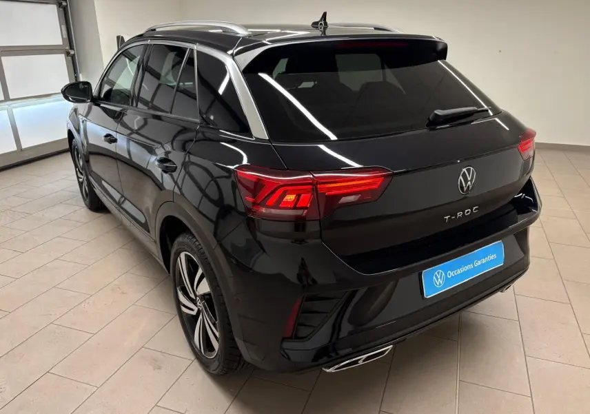 Vue 3/4 arrière droite du Volkswagen T-Roc noir intense 2025 avec feux arrière allumés et jantes R-Line visibles.