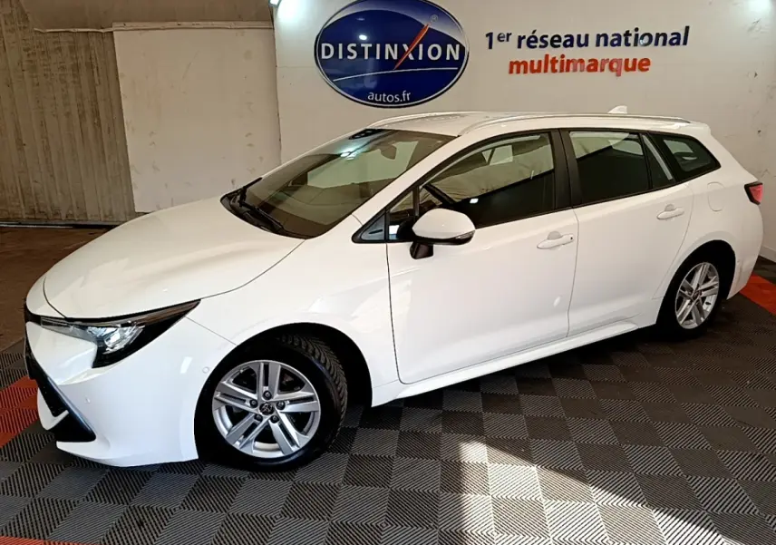 Toyota Corolla Hybride 122h Dynamic Business blanc vue de profil côté gauche en intérieur avec rails de toit chromés visibles.