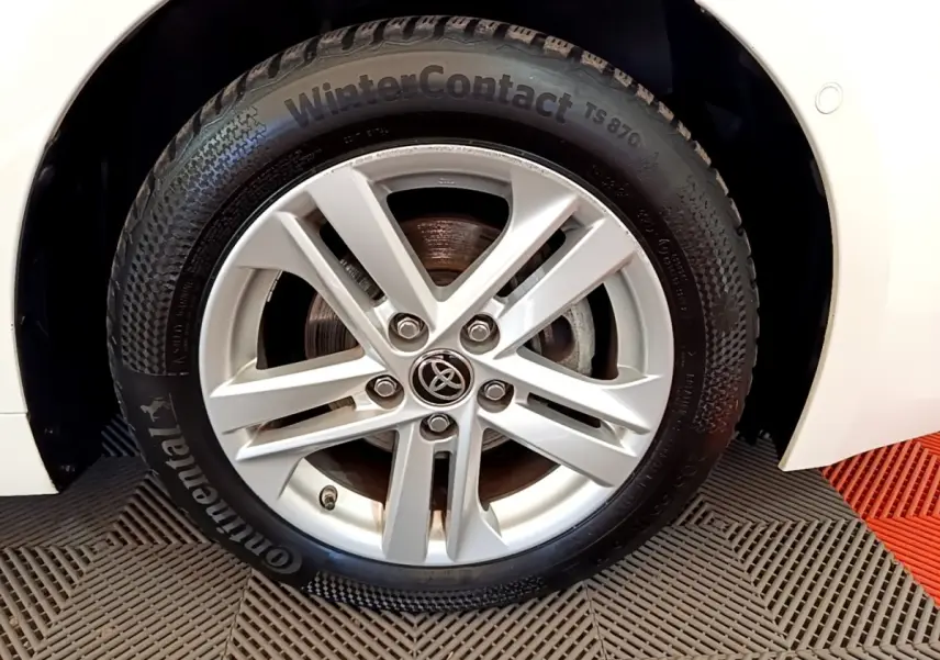 Gros plan sur la roue avant droite d'une Toyota Corolla hybride blanche, avec jante alliage et pneu hiver Continental.