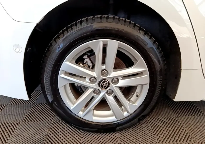 Gros plan sur la roue avant droite d'une Toyota Corolla blanche, mettant en valeur la jante alliage à cinq branches.