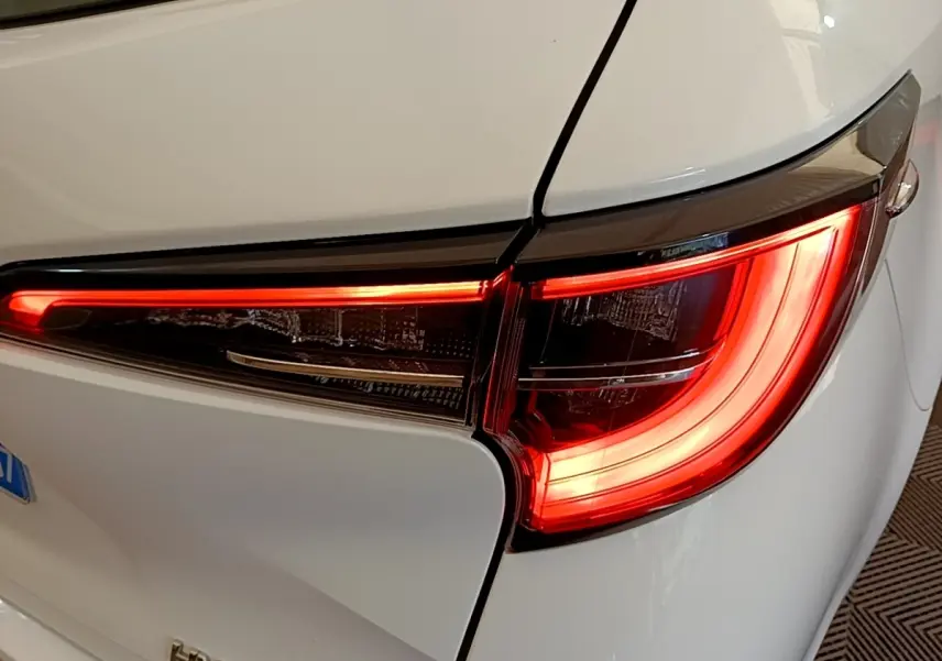 Gros plan sur le feu arrière droit allumé d'une Toyota Corolla hybride blanche de 2022, avec ligne lumineuse LED distinctive.