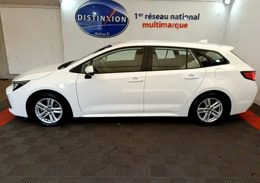 Vue latérale gauche d'une Toyota Corolla blanche hybride 2022 en break, avec rails de toit chromés visibles.