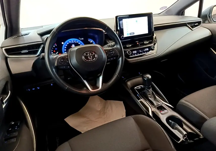 Intérieur de la Toyota Corolla hybride 2022 vu côté conducteur, volant cuir et écran tactile central lumineux.