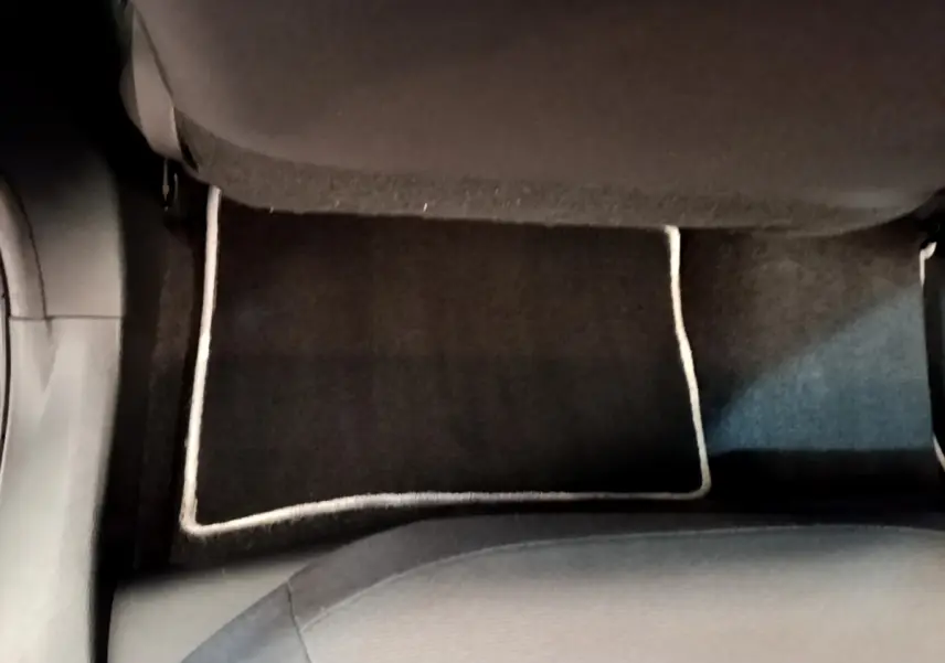 Vue plongeante sur le tapis de sol noir avec bordure claire à l'arrière d'une Toyota Corolla hybride blanche.