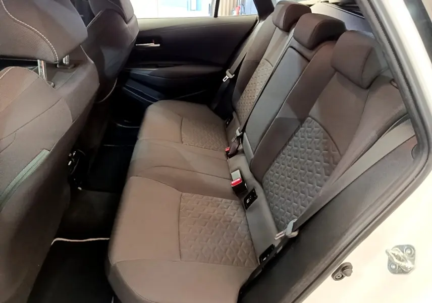 Vue intérieure côté droit sur la banquette arrière grise de la Toyota Corolla hybride blanche 2022 avec portes ouvertes.