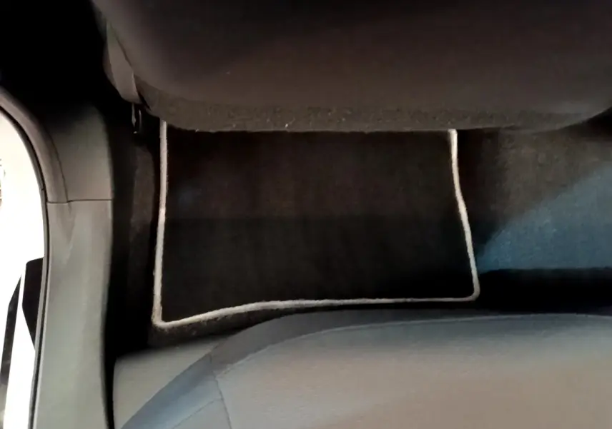 Vue plongeante sur le tapis de sol noir avec bordure claire et partie inférieure du siège avant d’une Toyota Corolla hybride blanche.