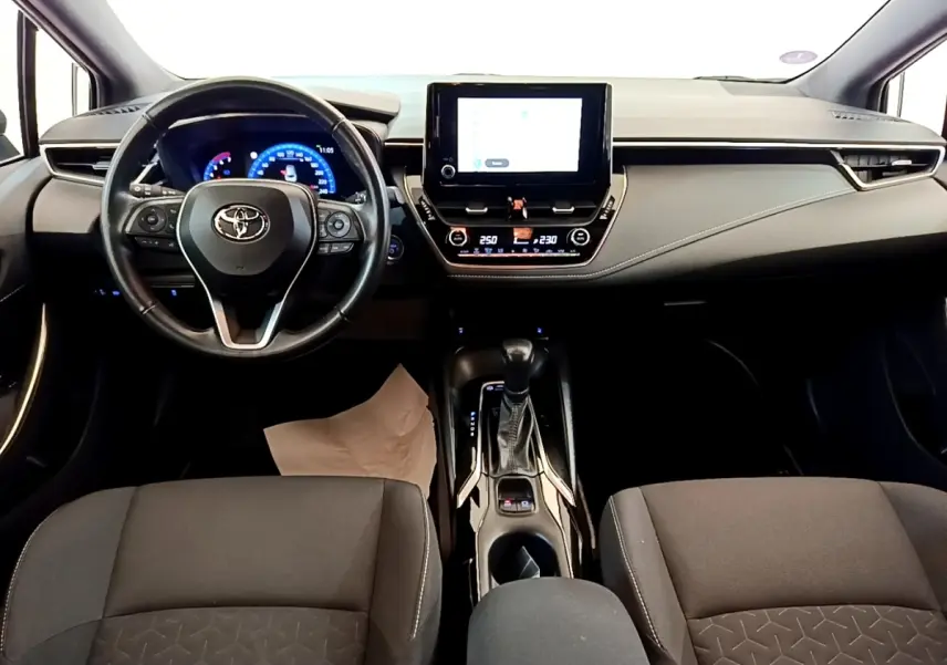 Vue intérieure avant de la Toyota Corolla Hybride 2022, tableau de bord noir avec écran tactile central et volant cuir multifonctions.