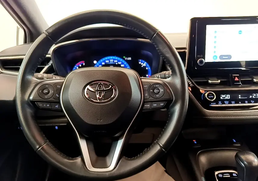 Vue intérieure centrée sur le volant cuir noir et le tableau de bord digital de la Toyota Corolla hybride 2022.
