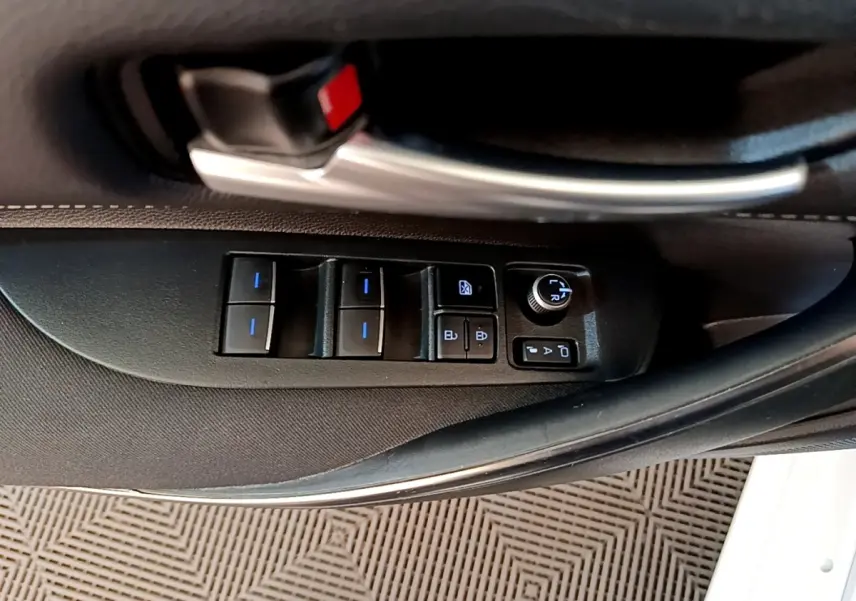 Gros plan sur la commande des vitres et rétroviseurs côté conducteur de la Toyota Corolla hybride blanche, intérieur noir.
