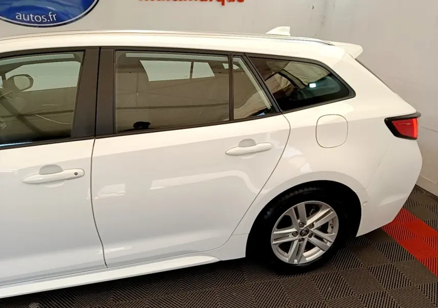 Vue latérale droite d'une Toyota Corolla hybride blanche, mettant en valeur les vitres teintées et les jantes alliage.