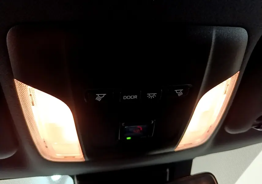 Plafonnier intérieur allumé avec commandes d’éclairage et bouton SOS dans une Toyota Corolla hybride blanche 2022.