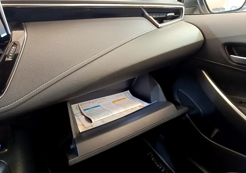 Intérieur côté passager de la Toyota Corolla hybride 2022, boîte à gants ouverte avec documents visibles, tableau de bord noir.