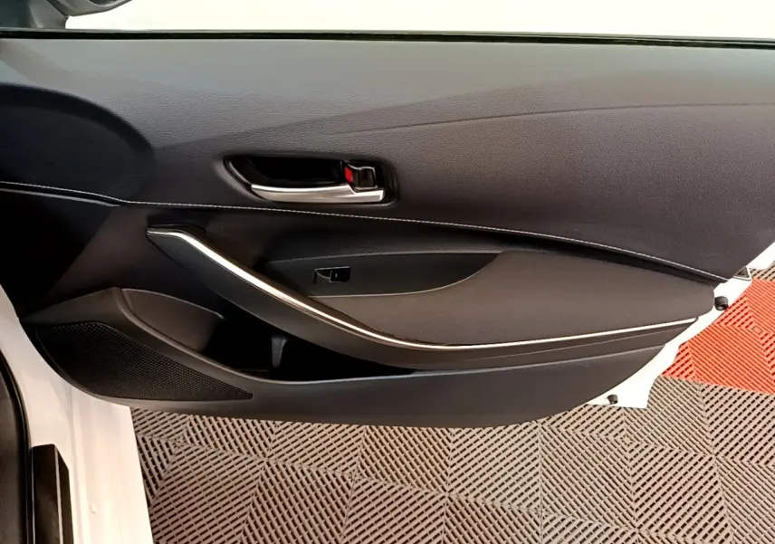 Vue intérieure côté gauche de la porte avant blanche d’une Toyota Corolla hybride avec poignée et garniture noire.