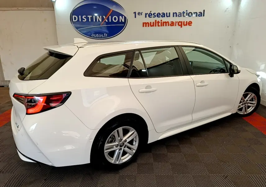 Toyota Corolla Hybride blanche vue de profil côté droit, avec feux arrière LED et rails de toit chromés visibles.