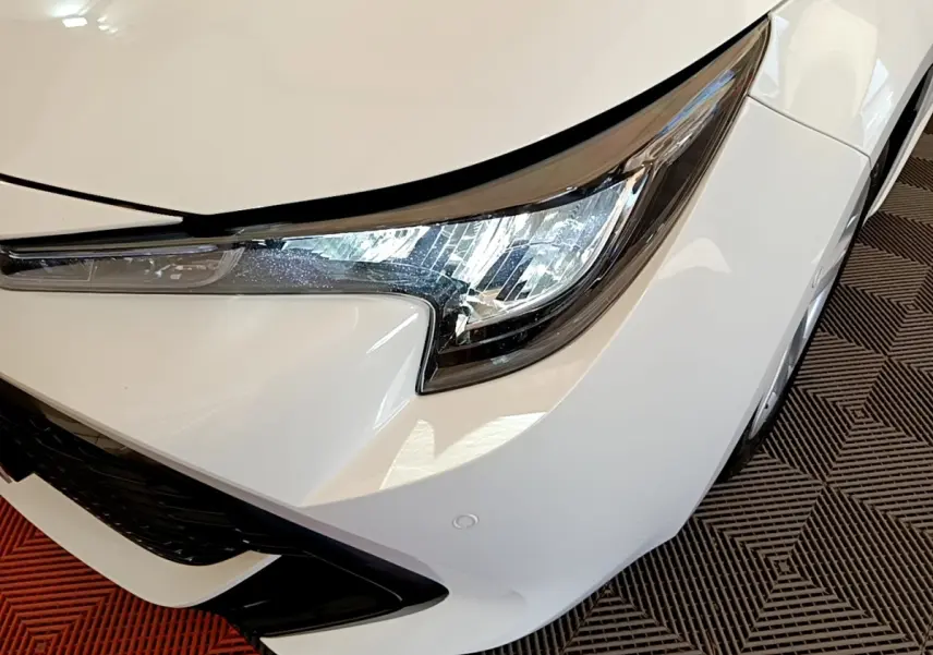 Gros plan sur l'avant droit blanc de la Toyota Corolla hybride 2022, mettant en valeur le phare LED et la calandre noire.