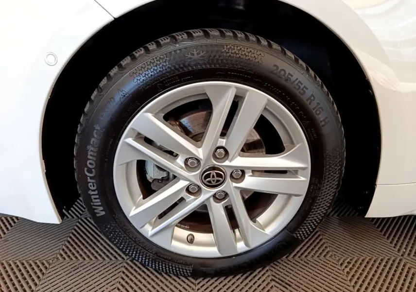 Gros plan sur la roue avant droite d'une Toyota Corolla blanche, jante alliage argentée et pneu hiver visible.