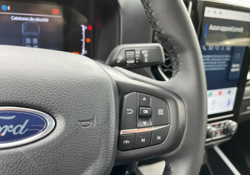 Gros plan sur le volant cuir multifonctions du Ford Ranger gris carbone, avec écran tactile et commandes au volant visibles.