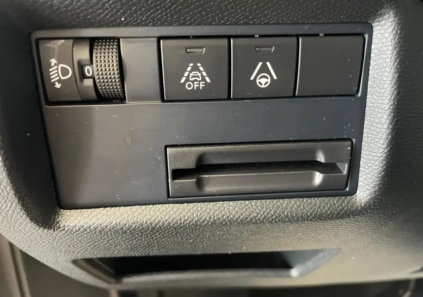 Gros plan sur les commandes noires du tableau de bord du Citroën C5 Aircross hybride 2025, avec réglage des phares et aides à la conduite.