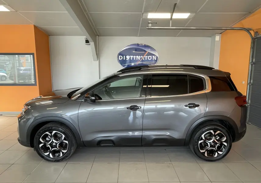 Vue latérale droite d'un Citroën C5 Aircross hybride gris platinium avec jantes alliage 18 pouces biton en intérieur showroom.