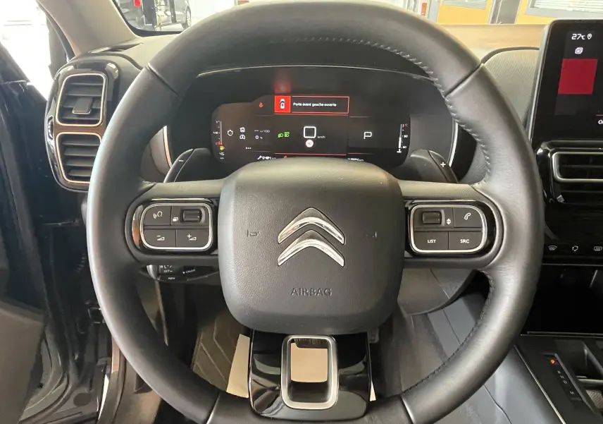 Vue rapprochée du volant en croûte de cuir noir du Citroën C5 Aircross hybride 2025, avec tableau de bord digital visible.