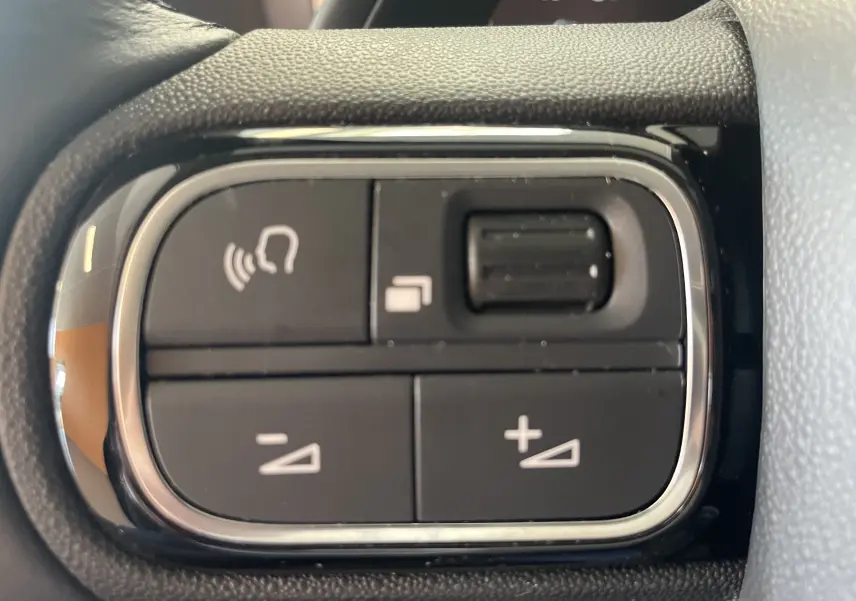 Gros plan sur les commandes au volant noir du Citroën C5 Aircross hybride 2025, boutons de réglage du volume et fonction mains libres.