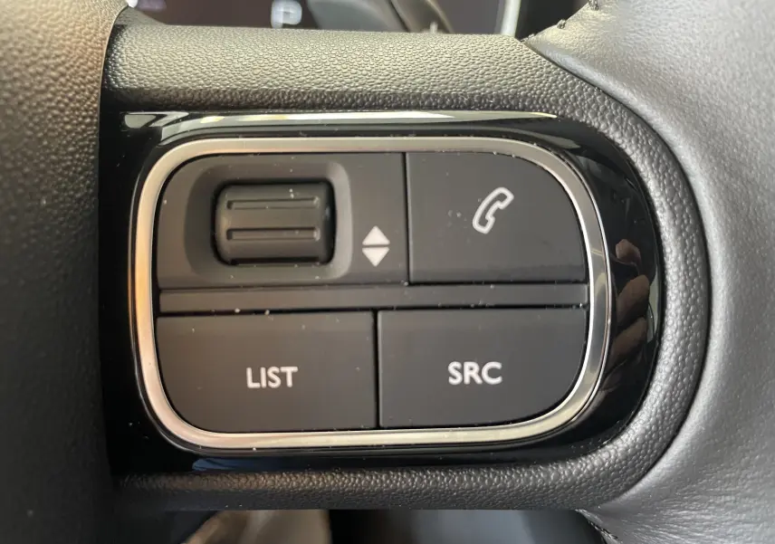 Gros plan sur les commandes noires du volant côté gauche du Citroën C5 Aircross hybride gris platinium 2025.