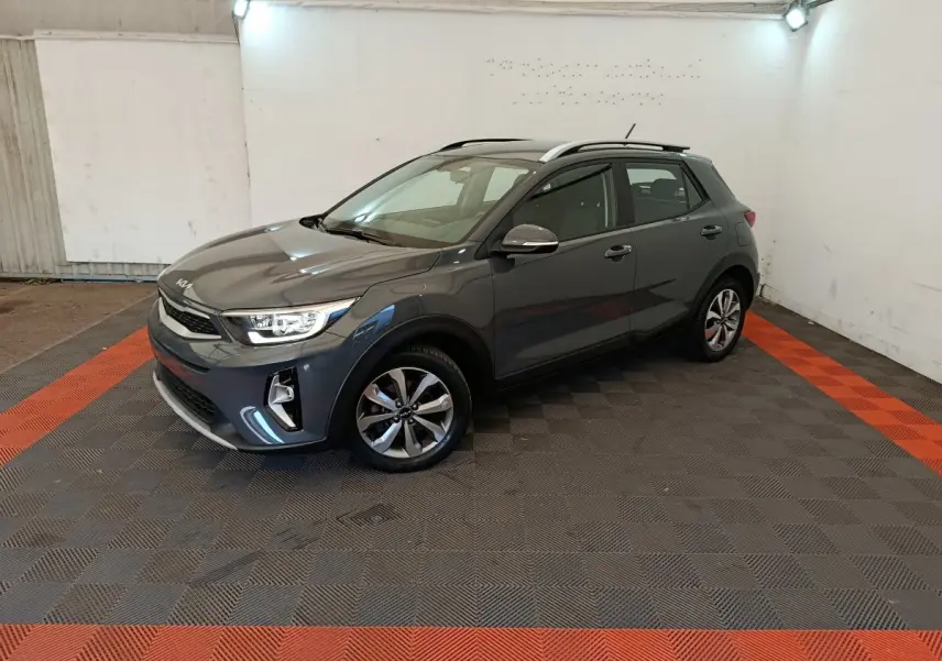 KIA Stonic gris foncé vue 3/4 avant droit dans un garage avec sol à damier noir et rouge.