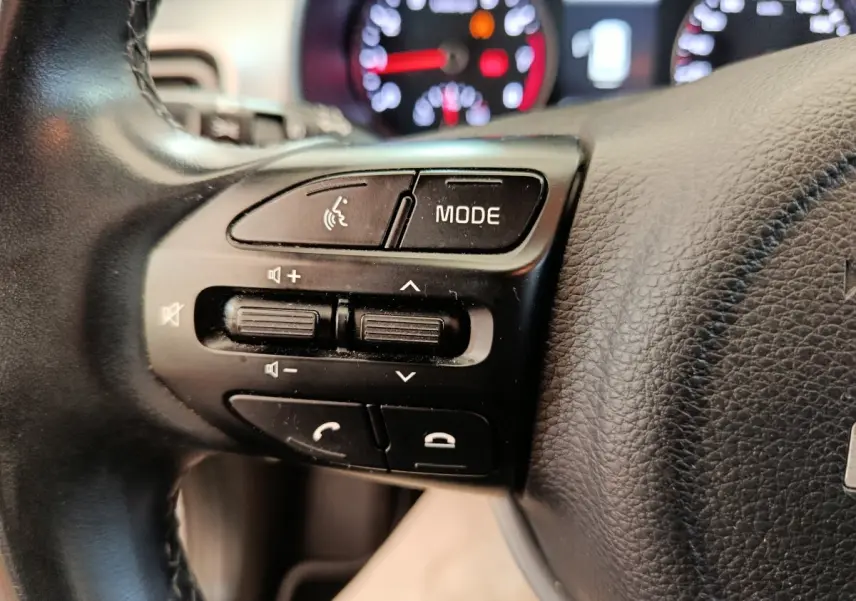 Gros plan sur les commandes du volant cuir noir de la Kia Stonic 2023, avec tableau de bord flou en arrière-plan.