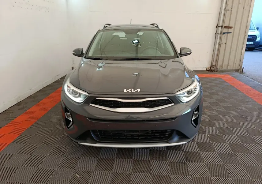 Vue frontale d'un KIA Stonic gris foncé 2023 avec phares allumés et calandre noire dans un garage.