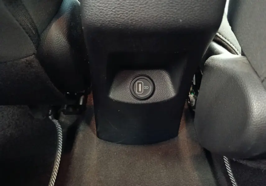 Prise USB arrière noire entre les sièges avant d’un Kia Stonic gris foncé, vue rapprochée du plancher.
