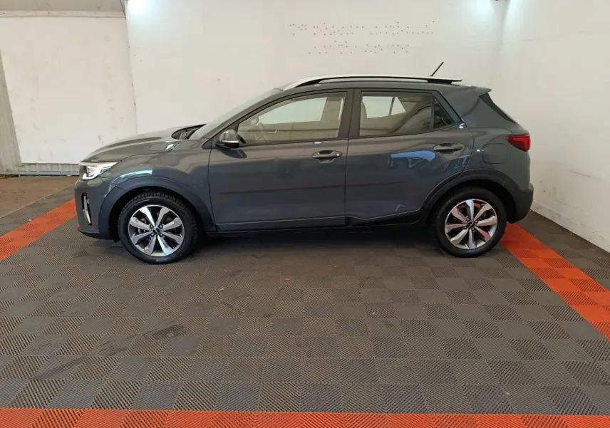 KIA Stonic gris foncé vu de profil côté gauche dans un garage avec sol à damier gris et rouge.