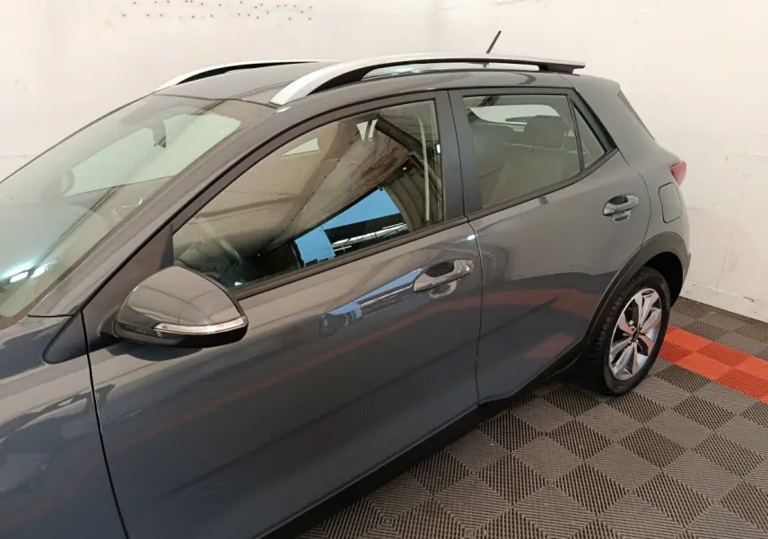 Vue latérale gauche d'un KIA STONIC gris foncé avec barres de toit blanches et jantes alliage.